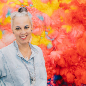 Smiling gray-haired woman by colorful fiber art