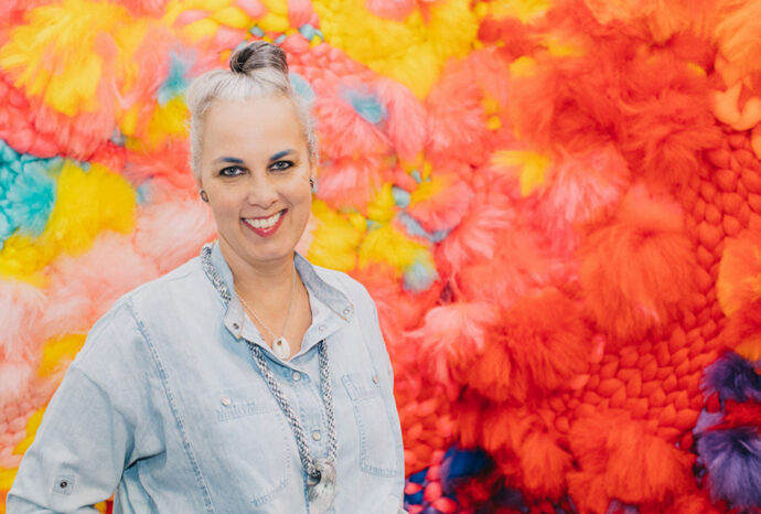 Smiling gray-haired woman by colorful fiber art