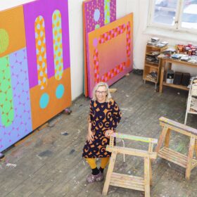 Artist in colorful studio surrounded by paintings
