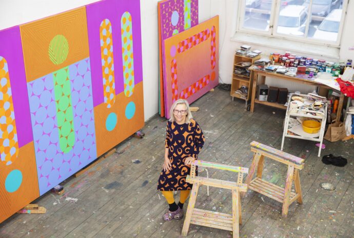 Artist in colorful studio surrounded by paintings